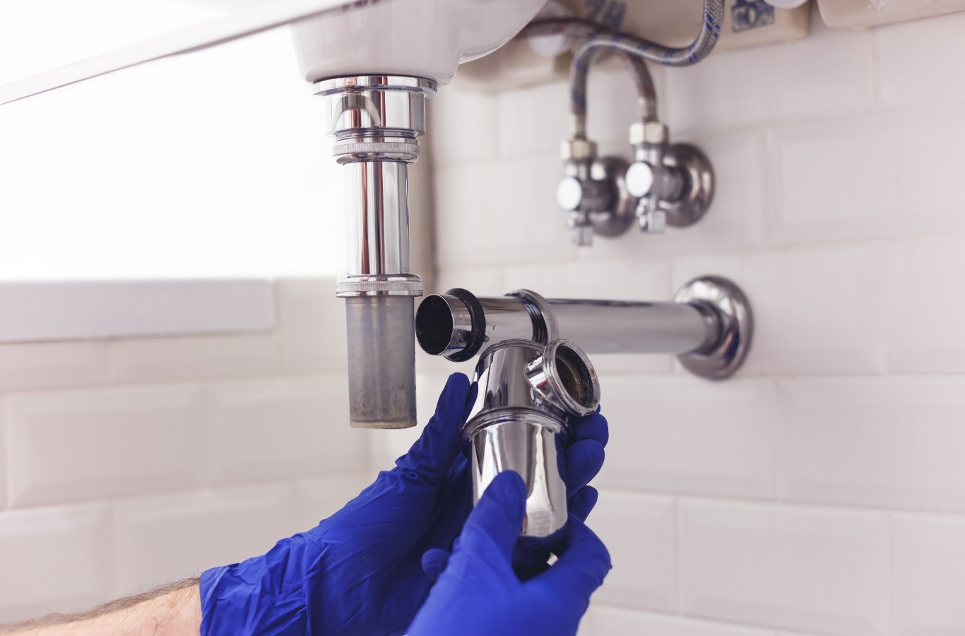 Blue-gloved hands removing a chrome sink trap, drain work by Starling Plumbing in Newport, TN. Plumber Near Me.