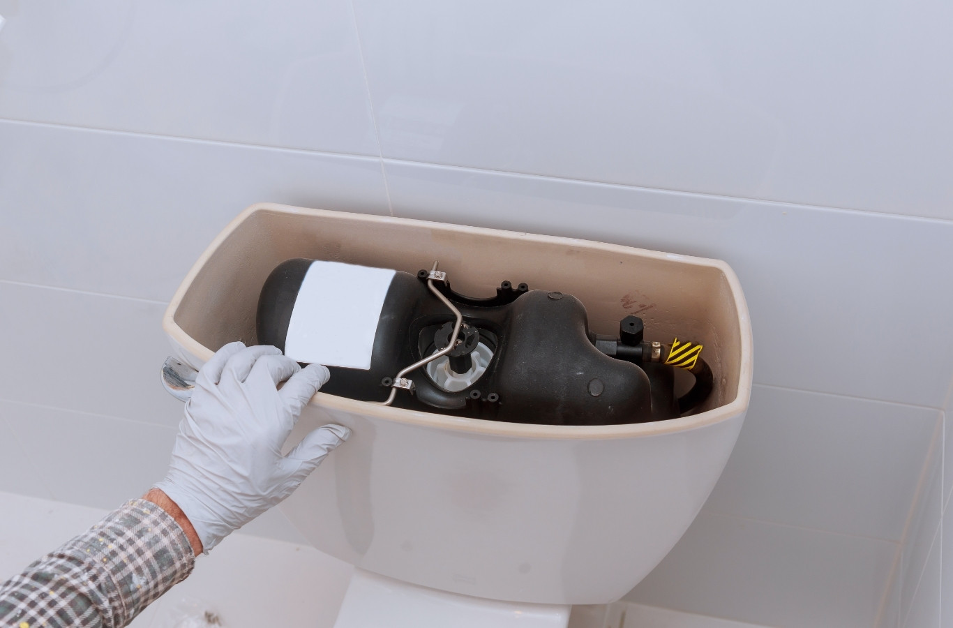 Gloved hand adjusting parts in a toilet tank, a repair by Starling Plumbing in Boyds Creek, TN. Plumber Near Me.