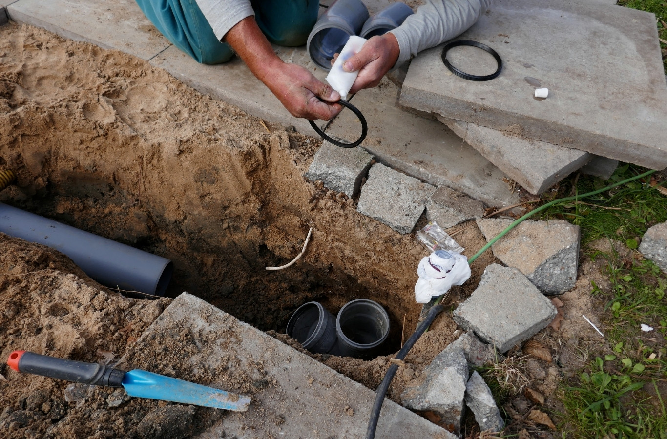 Hands fitting new drain pipe beside a trench, as Starling Plumbing does in Talbott, TN. Drain & Sewer Services Near Me.