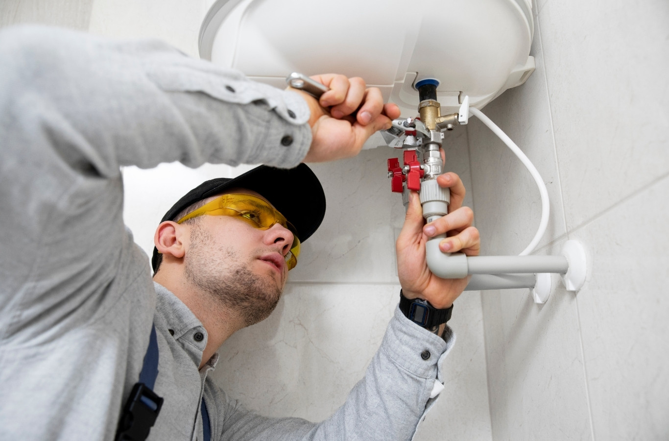 Plumber connecting water lines under a wall heater, as Starling Plumbing does in Sevierville, TN. Plumber Near Me.