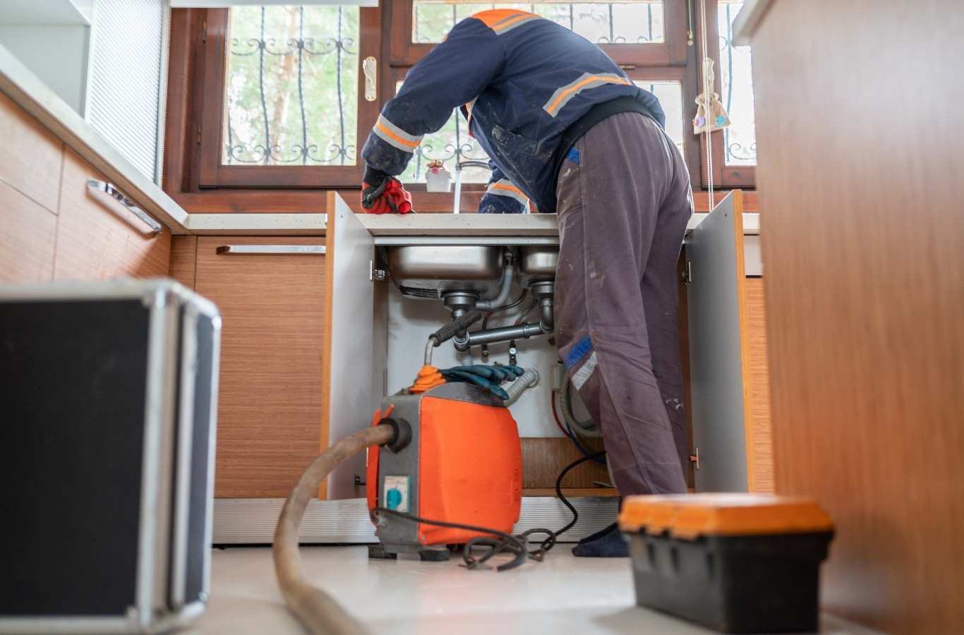 Plumber at an open sink cabinet with a drain machine on the floor, work Starling Plumbing does in Bean Station, TN