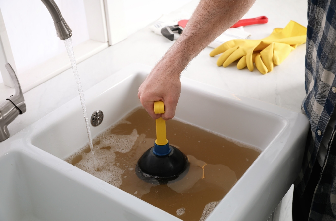 Plunger in a sink full of brown water under a running tap, a backup Starling Plumbing clears for Newport, TN families